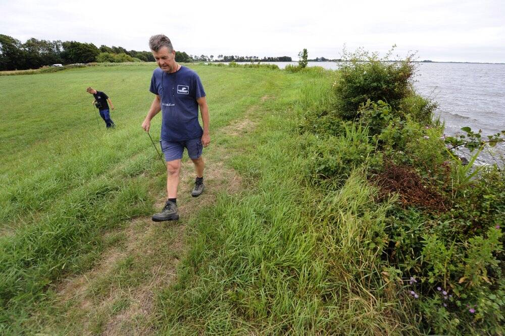 Met de meetstok op zoek naar scheuren in de polderdijk. Rayonbeheerder Gerrit Rijpkema van Wetterskip Fryslân (op de foto rechts) en zijn collega Harm Kuipers controleren momenteel honderden kilometers dijk. Het droge weer zorgt ervoor dat de zogeheten klei-op-veendijken door uitdroging scheuren en barsten kunnen ontstaan, waardoor de dijken kunnen doorbreken en het achterliggende land overstroomt. 